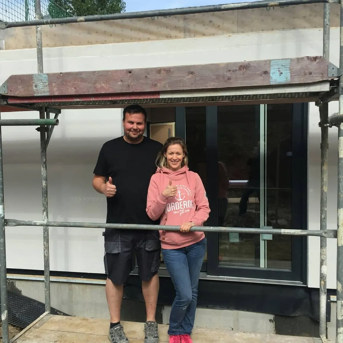 Paar steht auf einem Gerüst vor einem Haus welches gerade gebaut wird